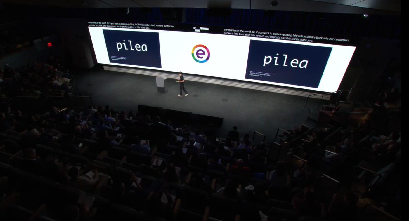 Baptiste on stage in front of a full auditorium, with the Pilea logo on the screen